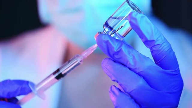 Doctor drawing up solution from vaccine bottle and filling syringe injection for patient vaccination in medical clinic, healthcare and medicine professional working