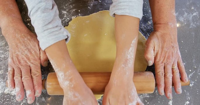 Grandmother and little girl hands flattening dough with rolling pin  