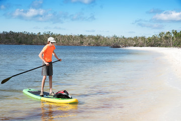 Fototapeta na wymiar A teenager on the paddle board approaches the sandy beach. Florida, USA