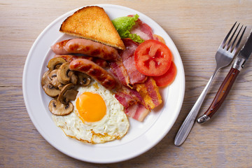 Traditional English or Irish breakfast: sausages, bacon, egg, mushrooms, tomatoes and toasts. Nutritious morning meal. View from above, top, horizontal