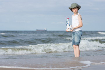 A guy with a toy wooden ship playing on the seashore.