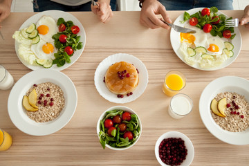 Dining table with food, couple enjoying delicious homemade meal together, man and woman have pancakes, eggs with salad and oatmeal on organic vegetarian breakfast, healthy eating lifestyle, top view