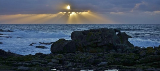 Côte, bord de l'océan ou de la mer avec rocher et coucher de soleil sur la mer avec des nuages et des rayons traversants