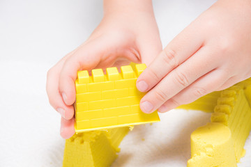 A child's hands playing with yellow magic sand and building, kneading at home. - 189382211