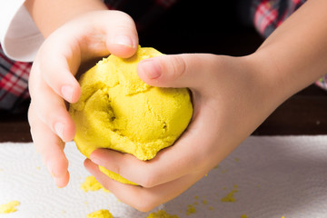 A child's hands playing with yellow magic sand and building, kneading at home. - 189382240