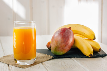 Mango and banana juice in glass over white wooden table.