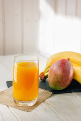 Mango and banana juice in glass over white wooden table.
