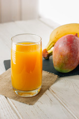Mango and banana juice in glass over white wooden table.