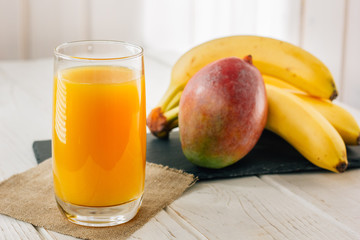 Mango and banana juice in glass over white wooden table.