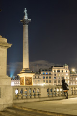 Night shot of Trafalgar Square with a girl from the back in the foreground, London.