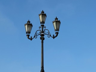 Fototapeta na wymiar City street lantern on the background of blue sky. Vintage iron street lamp isolated