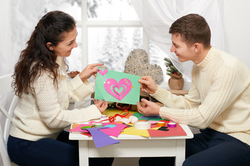 romantic young couple sit at the table and shows origami red heart, happy people and love concept