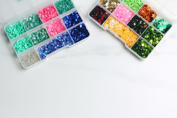 plastic box with sequin of different colors. marble light background, top view, space for text