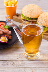 Glass of beer with burger and fries on wooden background. Beer and food concept. Ale and food. vertical