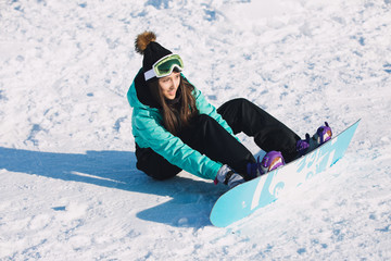 Leisure, winter, sport concept - snowboarder woman sitting and fasten board on legs