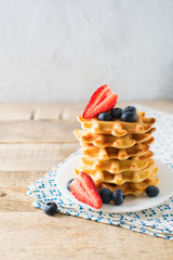 Stack of waffles with blueberries and strawberries on grey background