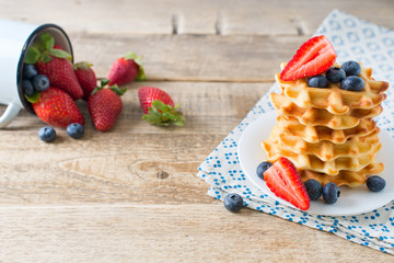 Stack of waffles with blueberries and strawberries on wooden background