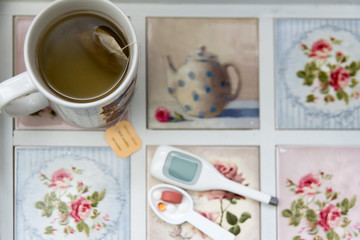 Cup of tea with tea bag on tray with digital thermometer, medicines and vitamins