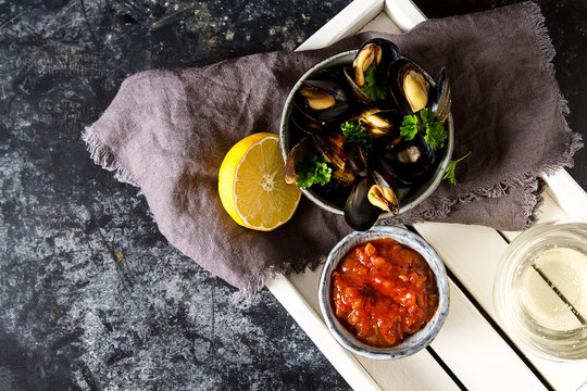 Mussels with herbs in a bowl with lemon and wine on a white wooden board. Seafood. Food at the shore of the French Sea. Dark background. Top view