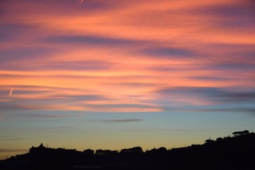 Tramonto con nuvole arancioni e rosa sulla collina
