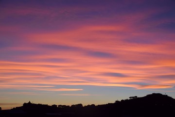 Tramonto con nuvole arancioni e rosa sulla collina