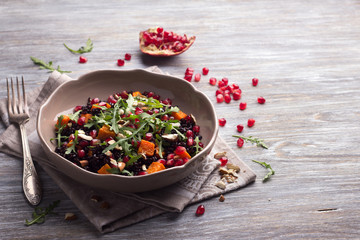 Salad with black rice, baked pumpkin, pomegranate seeds, arugula and nuts on a gray background with free space. Delicious vegan food