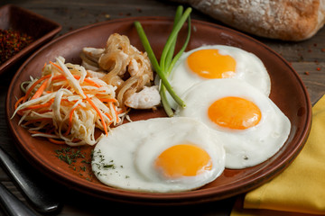 rustic plate of breakfast with two eggs and vegetables with chicken fillet on a wooden table