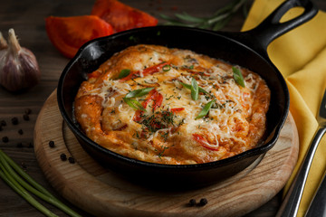 Hot pan with omelet and vegetables on a wooden table