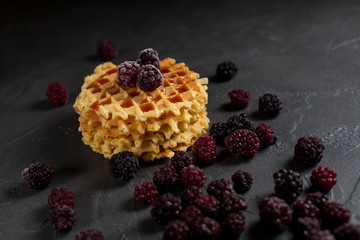 round fresh waffles with caramel and blackberry berries on a dark background