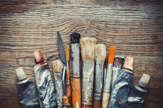 Artist paintbrushes, paint tubes and palette knife closeup on old wooden background, retro stylized. Copy space for text.