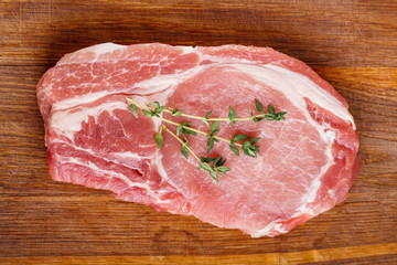 Raw pork natural cutlet with twigs of thyme on a wooden cutting board top view