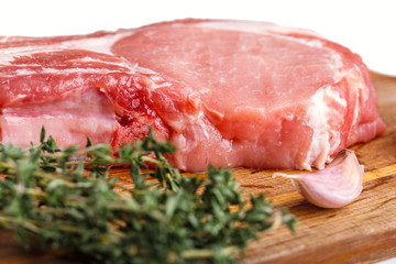 Raw pork natural cutlet with a bunch of thyme and a slice of garlic on a wooden cutting board close-up