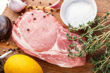 Raw pork natural cutlet with a bunch of thyme, garlic, salt, pepper and lemon on a wooden cutting board top view