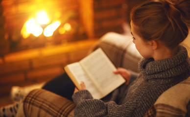 young woman   reading a book by the fireplace on a winter evening.