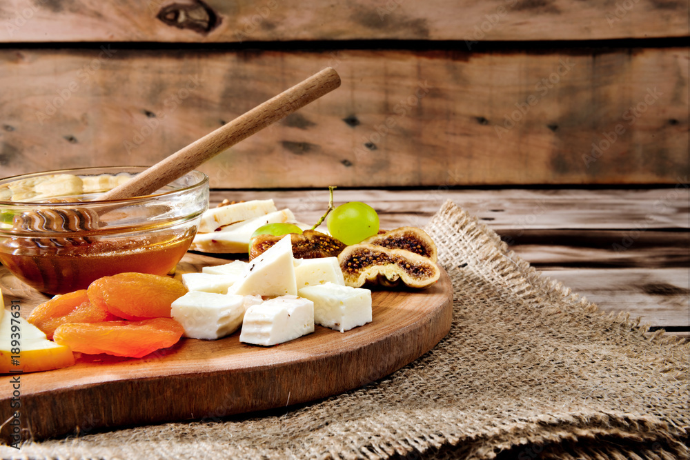 Wall mural cheese plate - various types of cheese, honey, grapes, dried apricots, nuts and figs on a wooden boa