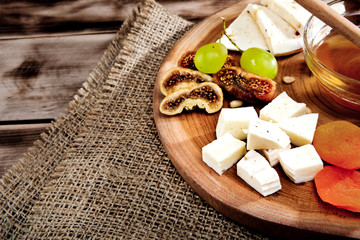 Cheese plate - various types of cheese, honey, grapes, dried apricots, nuts and figs on a wooden board on dark wooden background.