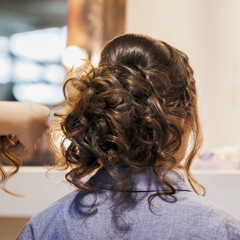 Fototapeta premium Unrecognizable girl back to us, young woman in mirror at hairdresser making hairstyle, styling from long hair in hair salon. Hands of master are partially visible