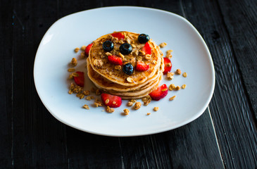 Homemade pancakes with fresh berries, strawberries, blueberries and maple syrup on a dark wooden background.