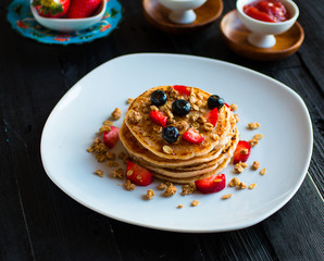 Homemade pancakes with fresh berries, strawberries, blueberries and maple syrup on a dark wooden background.
