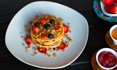Homemade pancakes with fresh berries, strawberries, blueberries and maple syrup on a dark wooden background.