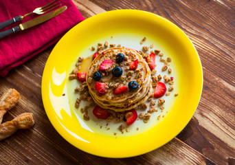 Homemade pancakes with fresh berries, strawberries, blueberries and maple syrup on a wooden background.