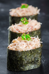Three Gunkan maki sushi with crab meat and sauce spice on black background