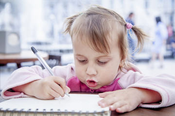 little beautiful child girl learns to write outdoors (preschool, development, training, education concept)