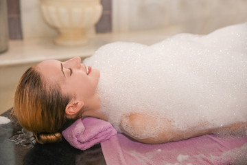 Young woman covered with foam in hammam