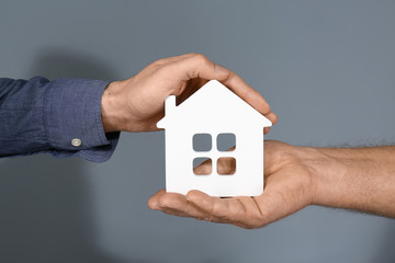 Real estate agent and senior man holding house model on grey background
