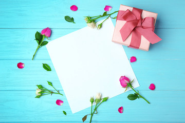 Sheet of paper, roses and gift box on wooden background