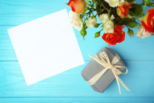 Roses, sheet of paper and gift box on wooden background