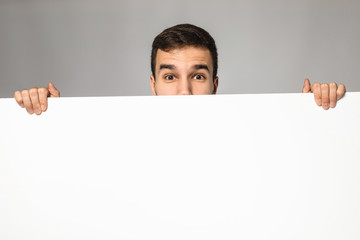 Handsome businessman with blank advertising board on grey background