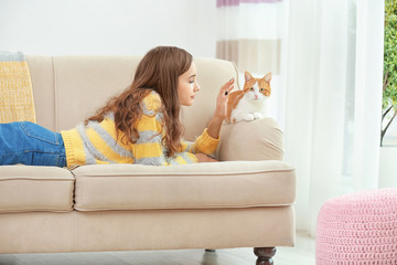 Beautiful young woman with cute cat on sofa at home