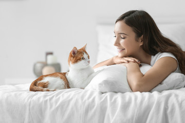 Beautiful young woman with cute cat on bed at home